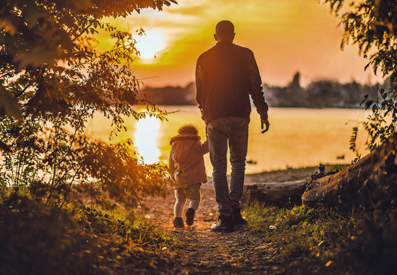 Photo of a man walking with a child while looking at a sunset