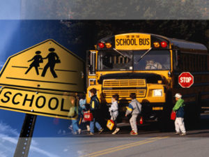 Photo of kids walking in a line in front of a school bus