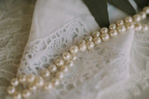 Photo of a white, laced handkerchief with a pearl necklace on top of it